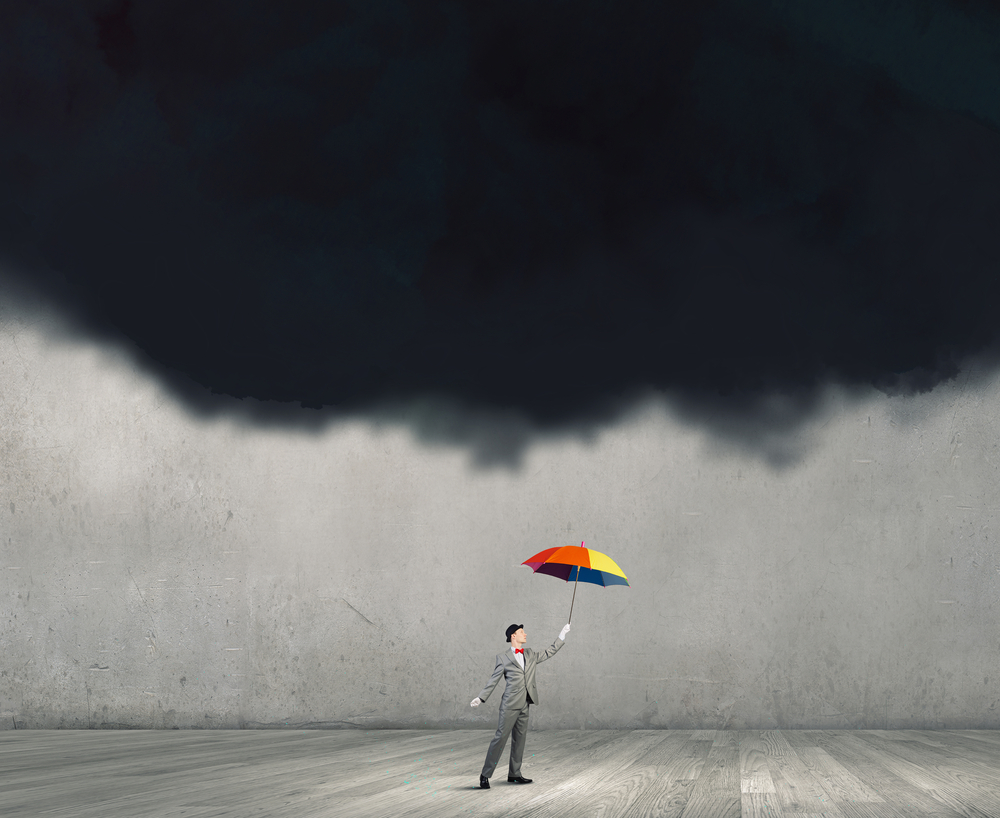 Businessman standing with umbrella under black cloud