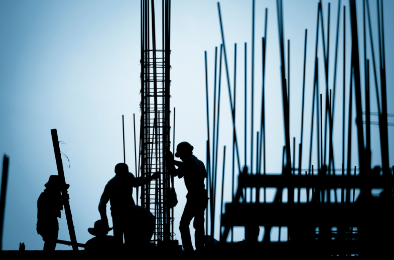 Silhouette of two construction workers in front of a building frame