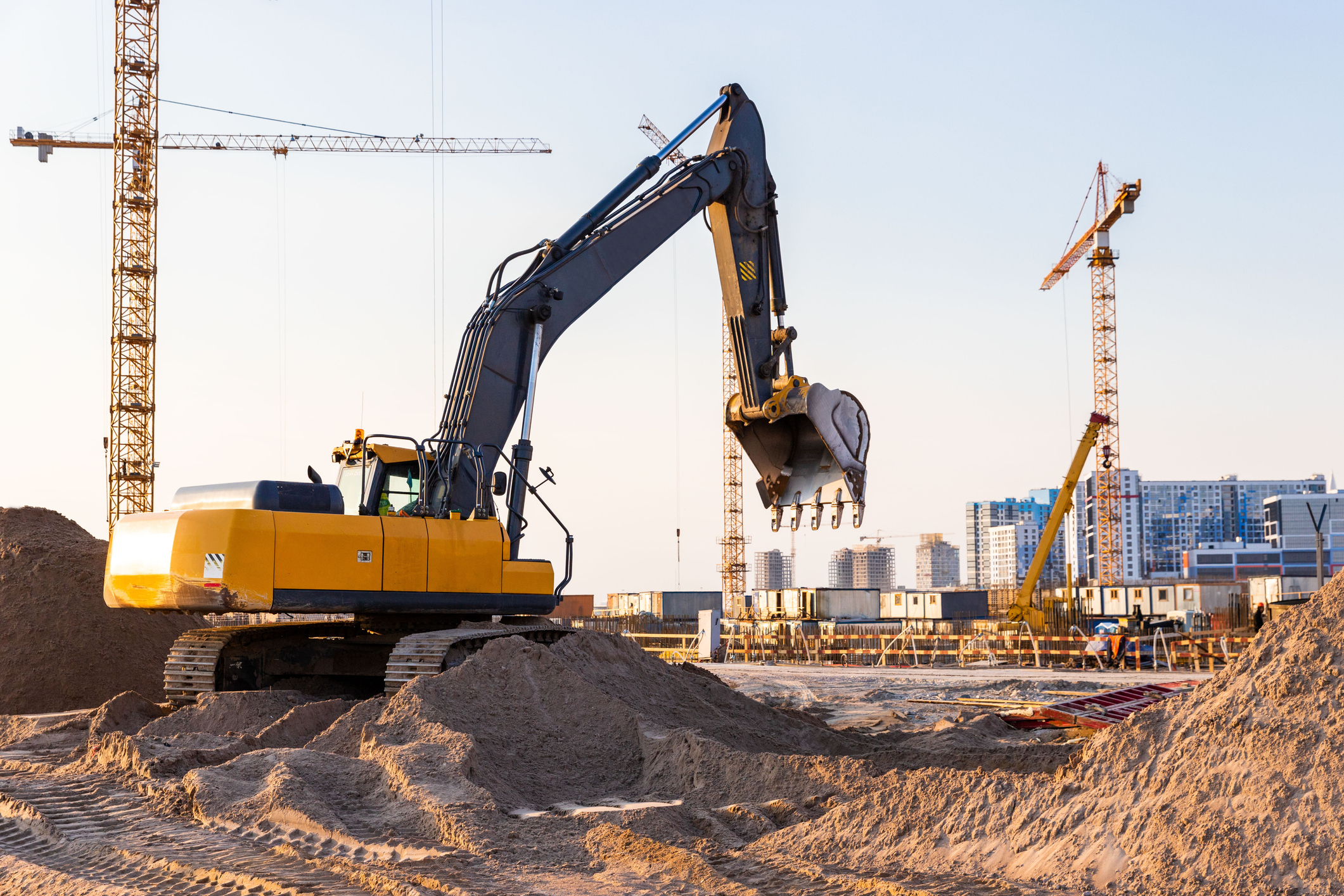 Group tower cranes and excavator silhouette at construction site